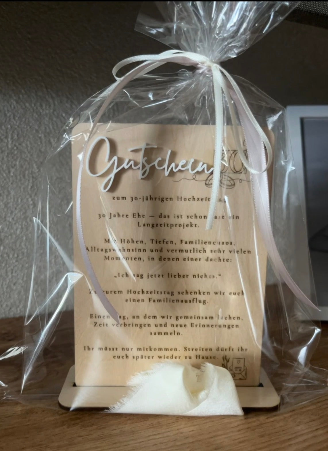 Verpackter Gutschein-Holzaufsteller mit weißem erhabenem Schriftzug, persönlicher Gravur und heller Schleife.