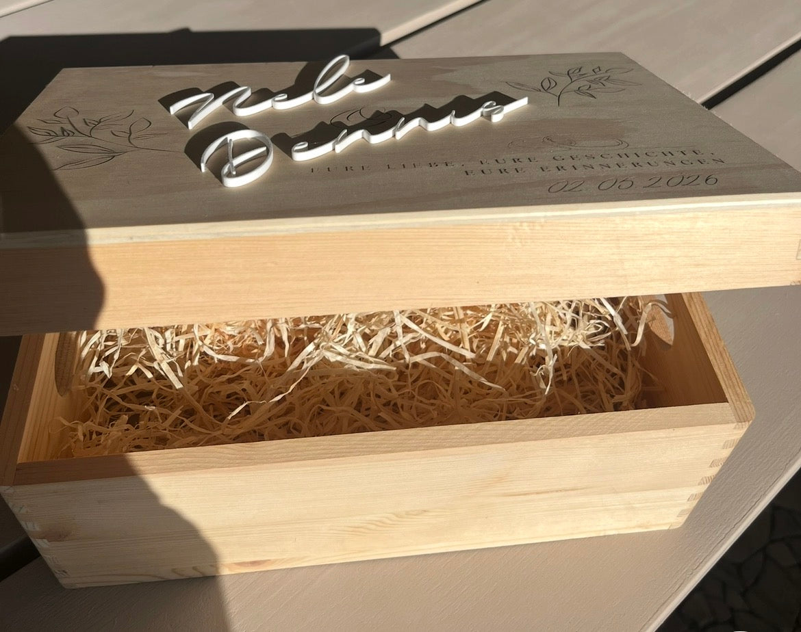 Geöffnete personalisierte Holzbox mit Füllmaterial und einem Deckel mit weißen aufgesetzten Namen.