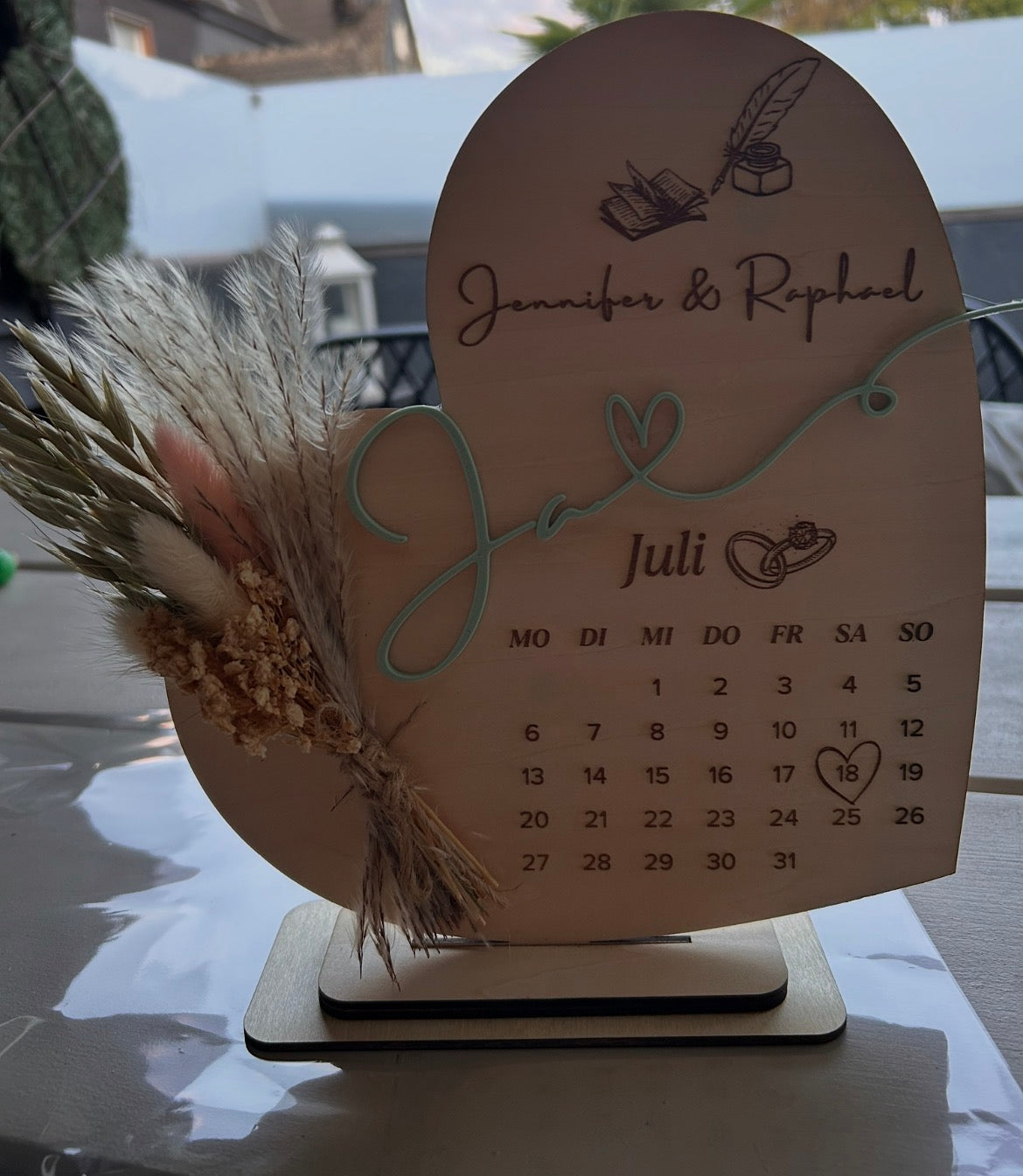 Holzaufsteller zur Hochzeit mit zwei Namen, graviertem Kalender, markiertem Datum und Trockenblumen.