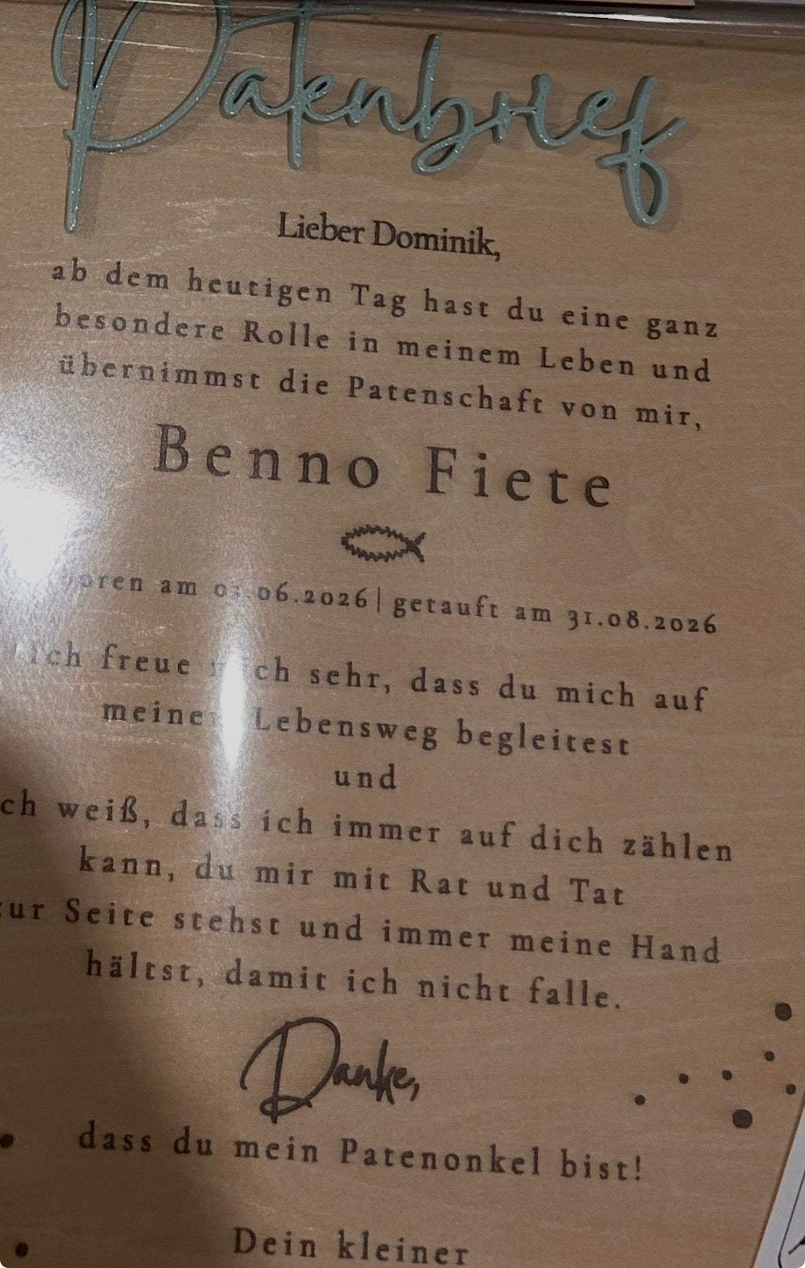 Detail eines Patenbriefs aus Holz mit graviertem Text und aufgesetztem hellgrünem Schriftzug.
